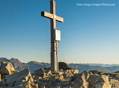 Ein Kreuz auf einem Gipfel vor blauem Himmel