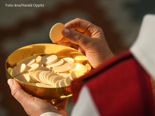 Ein Priester teilt Hostien aus einem goldenen Kelch aus. 