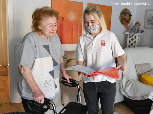 Eine Mitarbeitern der Ambulanten Pflege der Caritas trägt Mundschutz und spricht mit einer Patientin in deren Wohnung in Bonn.