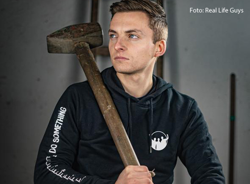 Phillip Mickenberger hält einen großen Hammer in der Hand. Erveröffentlicht Videos auf Youtube, in denen er verrückte Objekte baut.