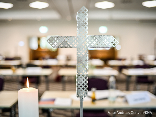 Eine brennende Kerze und ein gelochtes Metallkreuz vor dem noch leeren Tagungsraum der Regionenkonferenz "Fünf Orte - ein Weg" zum synodalen Weg am 4. September 2020 in Dortmund.