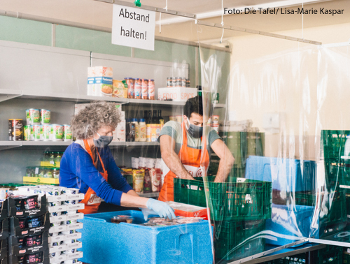 Helfer der Tafel sortieren Lebensmittel. Sie tragen dabei Corona-Schutzmasken. 