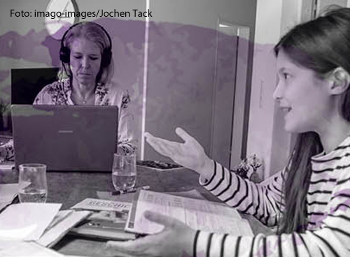 Eine Frau sitzt mit ihrer Tochter an einem Tisch. Beide arbeiten.