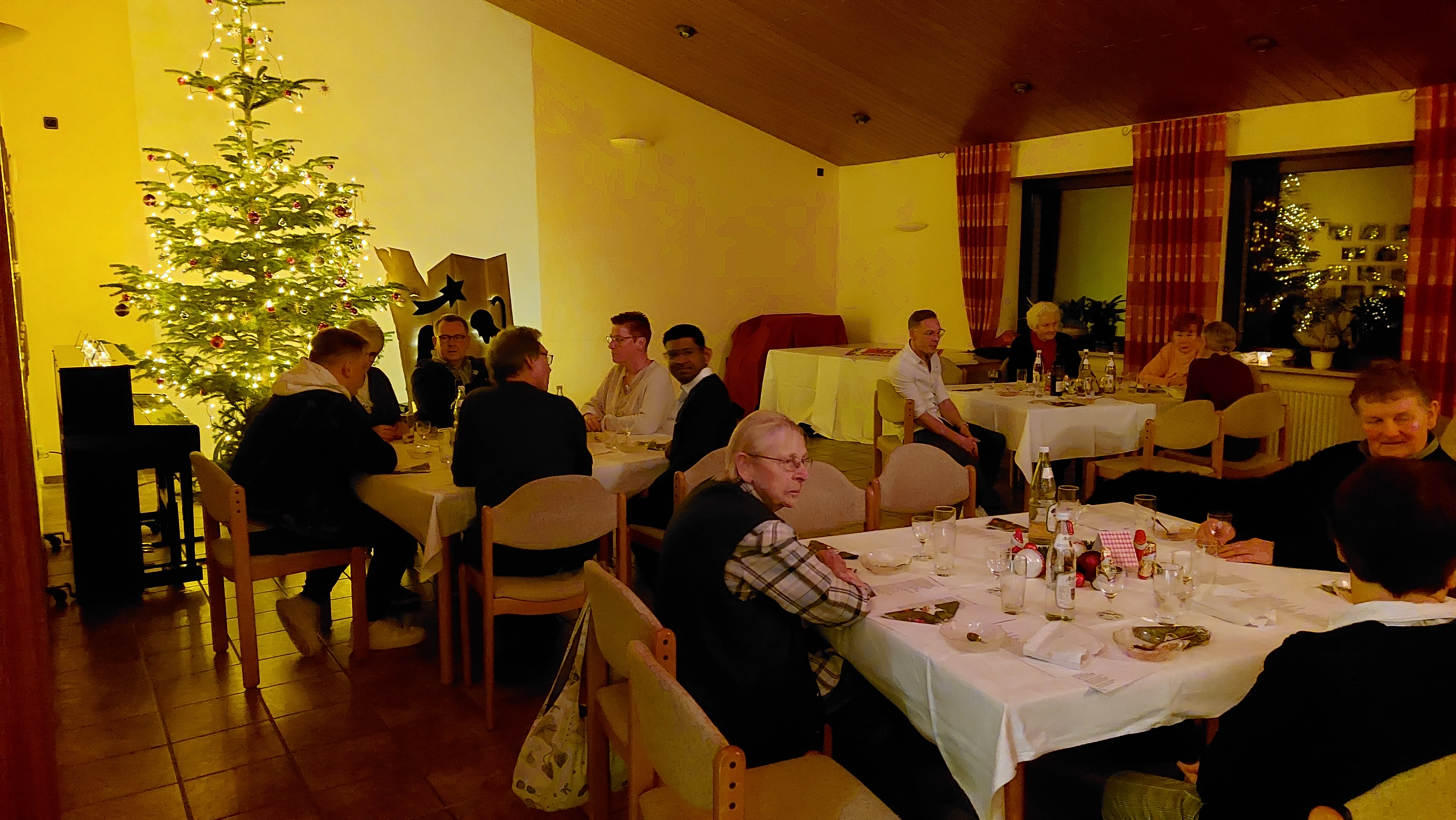 Menschen sitzen an Tischen, im Hintergrund ein Weihnachtsbaum