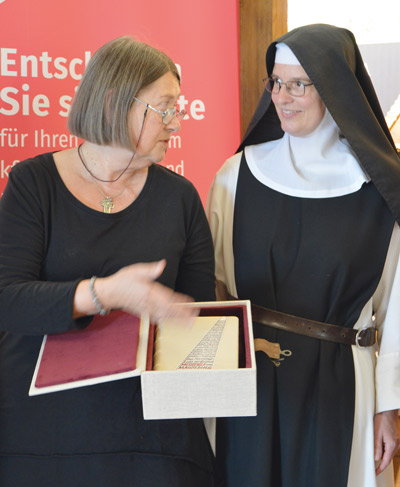 eine Frau übergibt ein Buch an eine Nonne