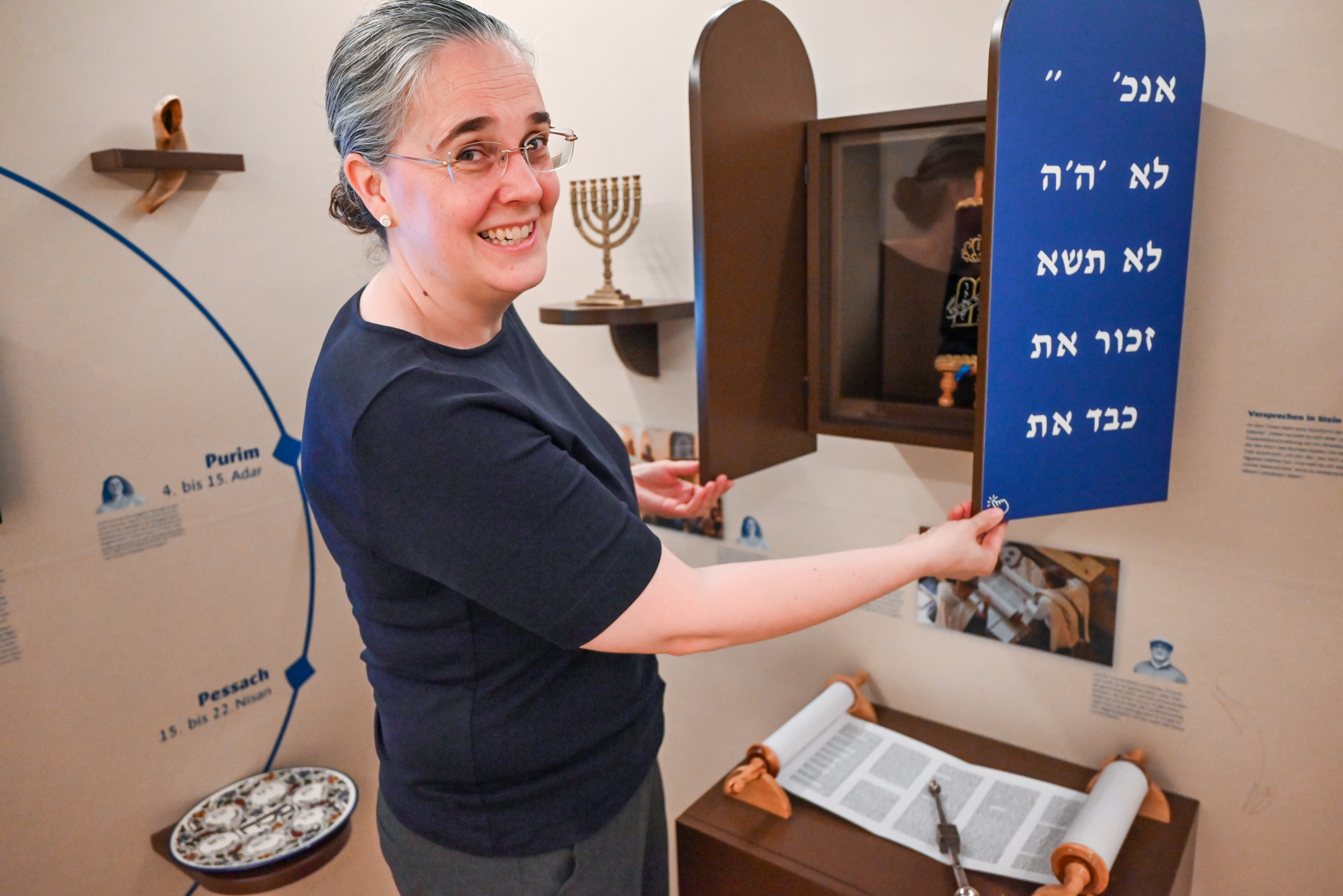 Rebekka Brouwer öffnet einen kleinen hölzernen Schrein, in dem eine Thora-Rolle abgelegt ist. Sie lächelt in die Kamera.