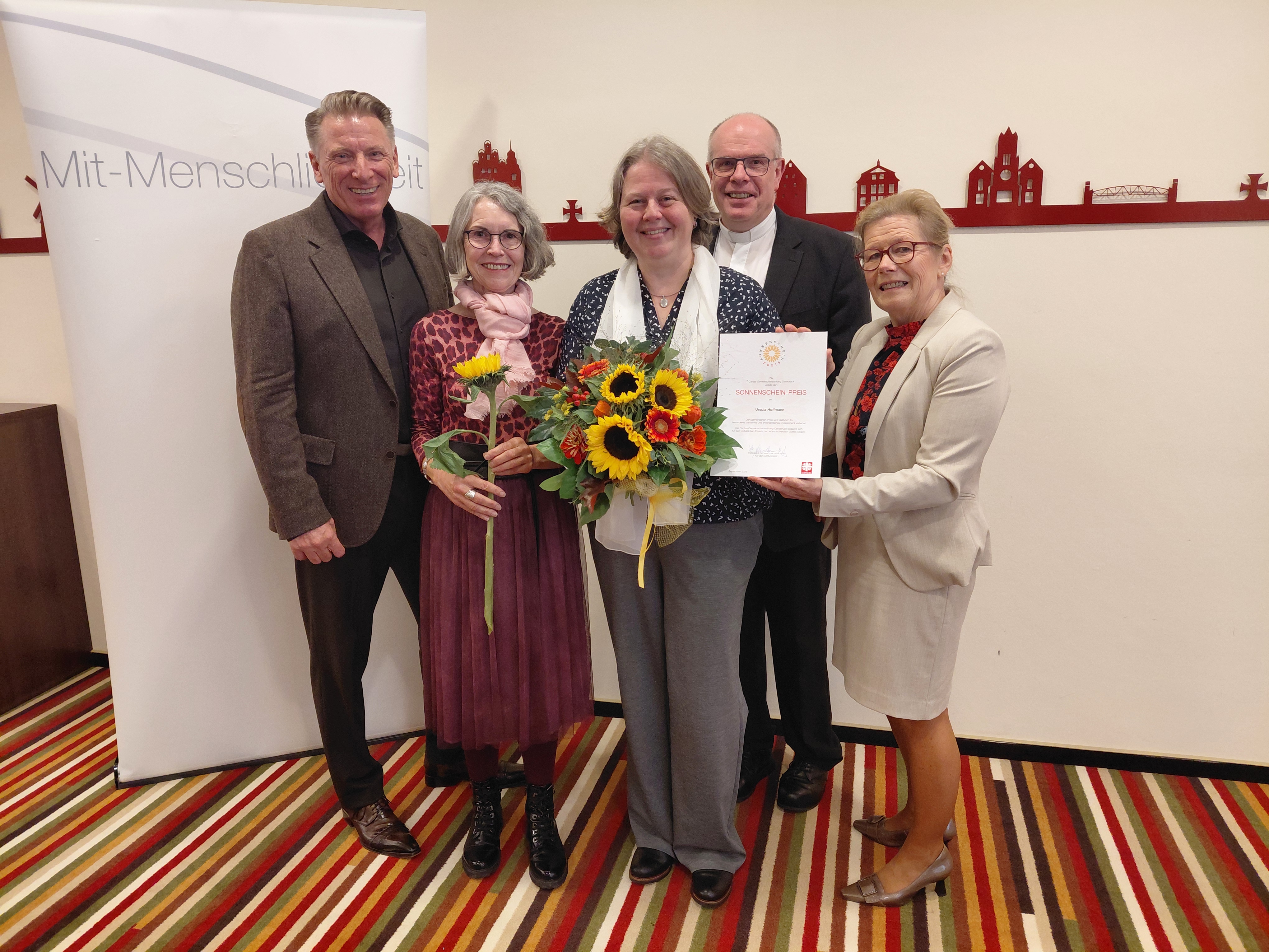 Sechs ältere Menschen vor einer Caritas-Fotowand mit einer Sonnenblume
