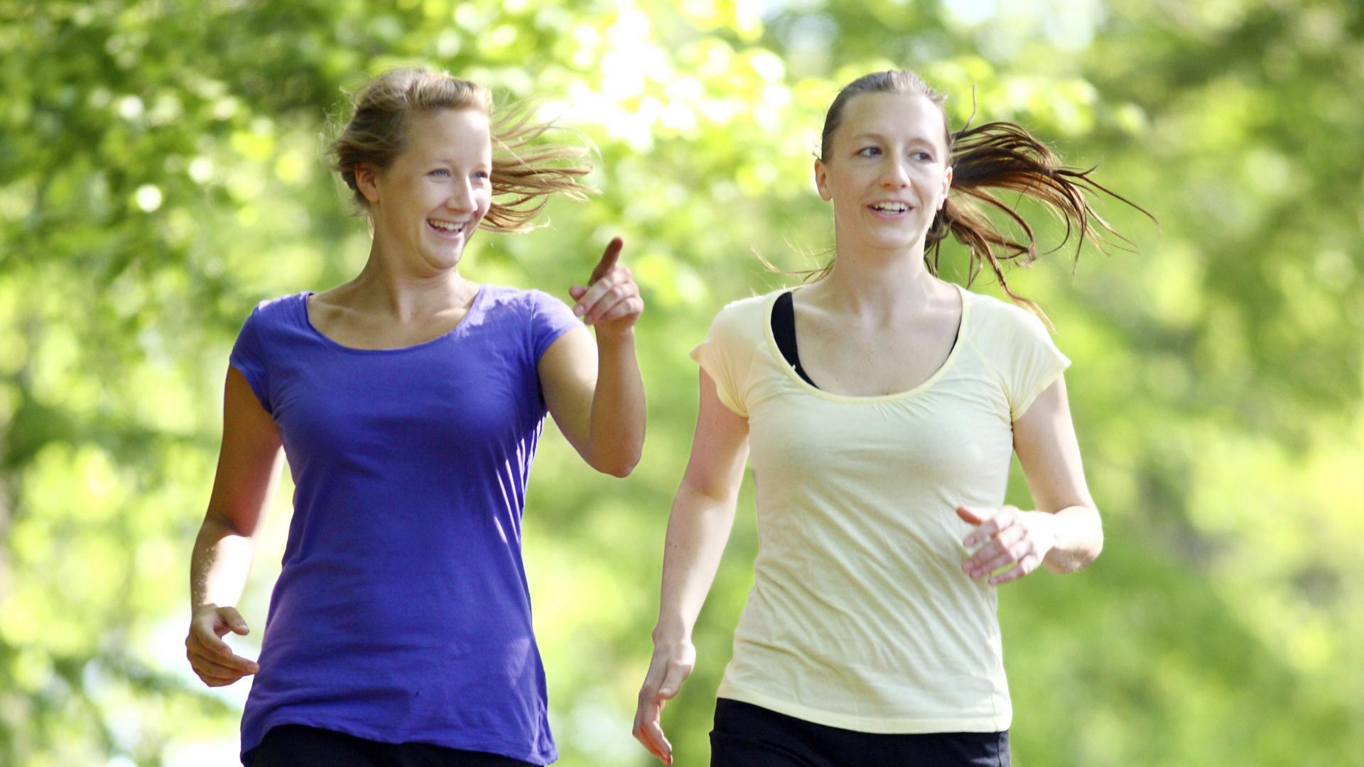 Zwei Frauen in Sportkleidung laufen fröhlich durch die Natur