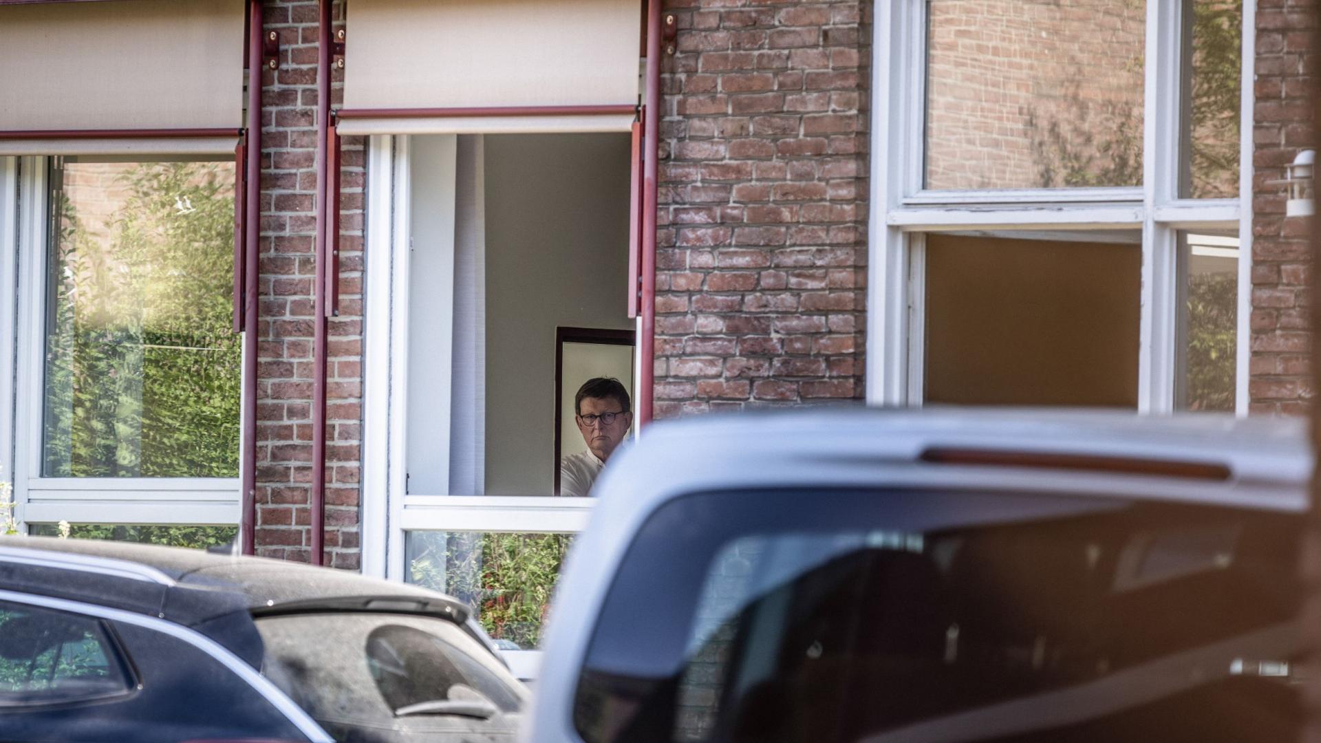 Kardinal Rainer Maria Woelki blickt versteckt durch ein Fenster, im Vordergrund sind Fahrzeuge zu sehen