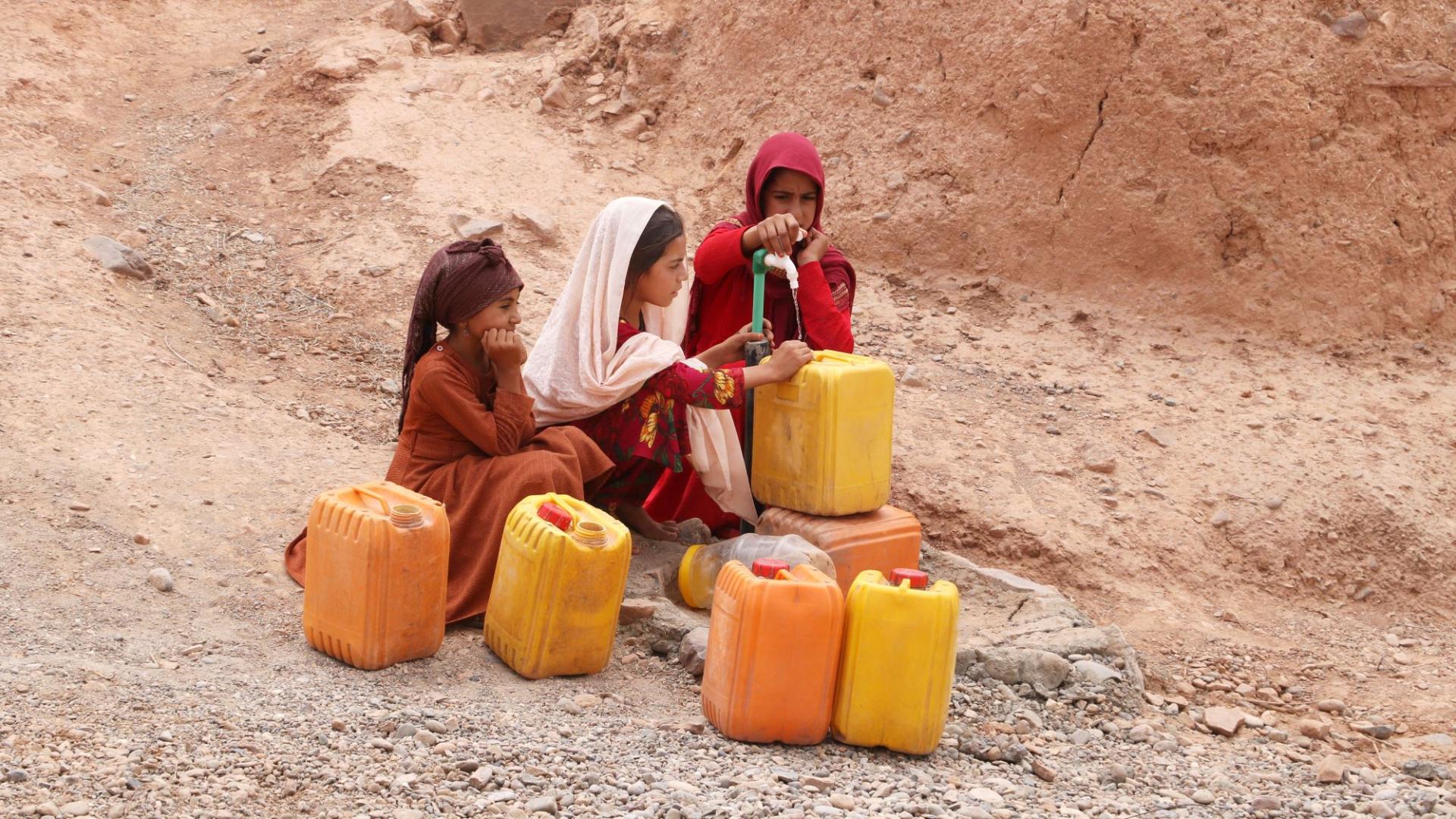 Drei Mädchen hocken an einem Brunnen in Afghanistan um Wasser in Kanister zu füllen