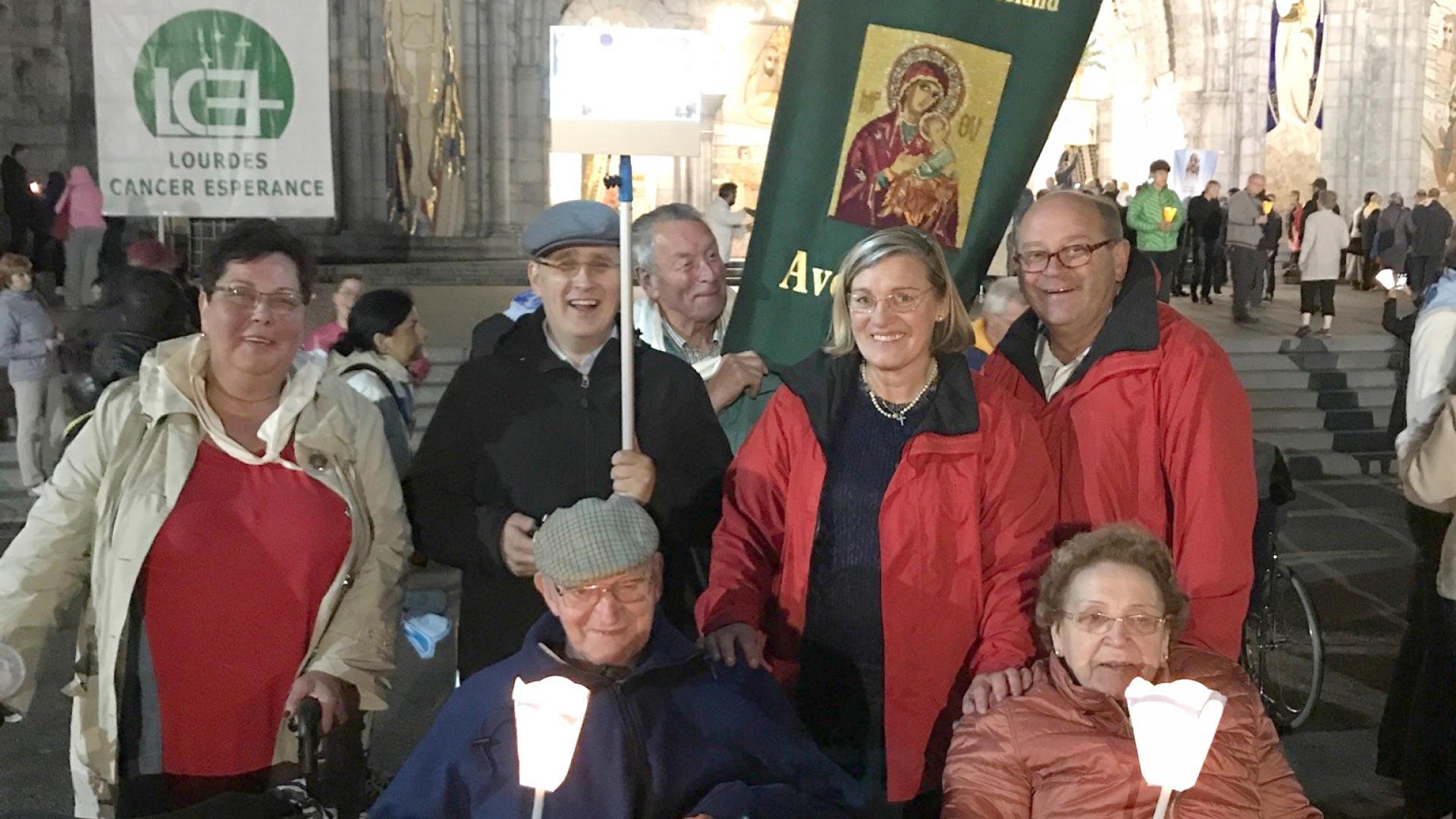 Mehrere Menschen mit Kerzen und Bannern in Lourdes.