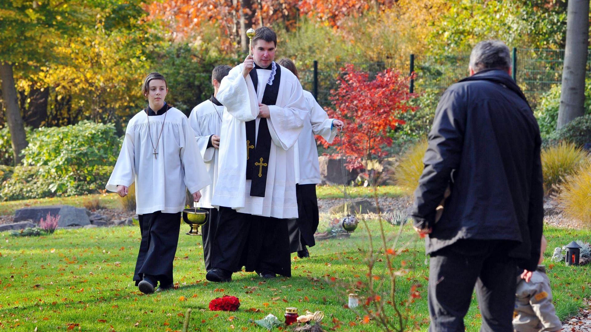 Ein Priester geht segnend über einen Friedhof