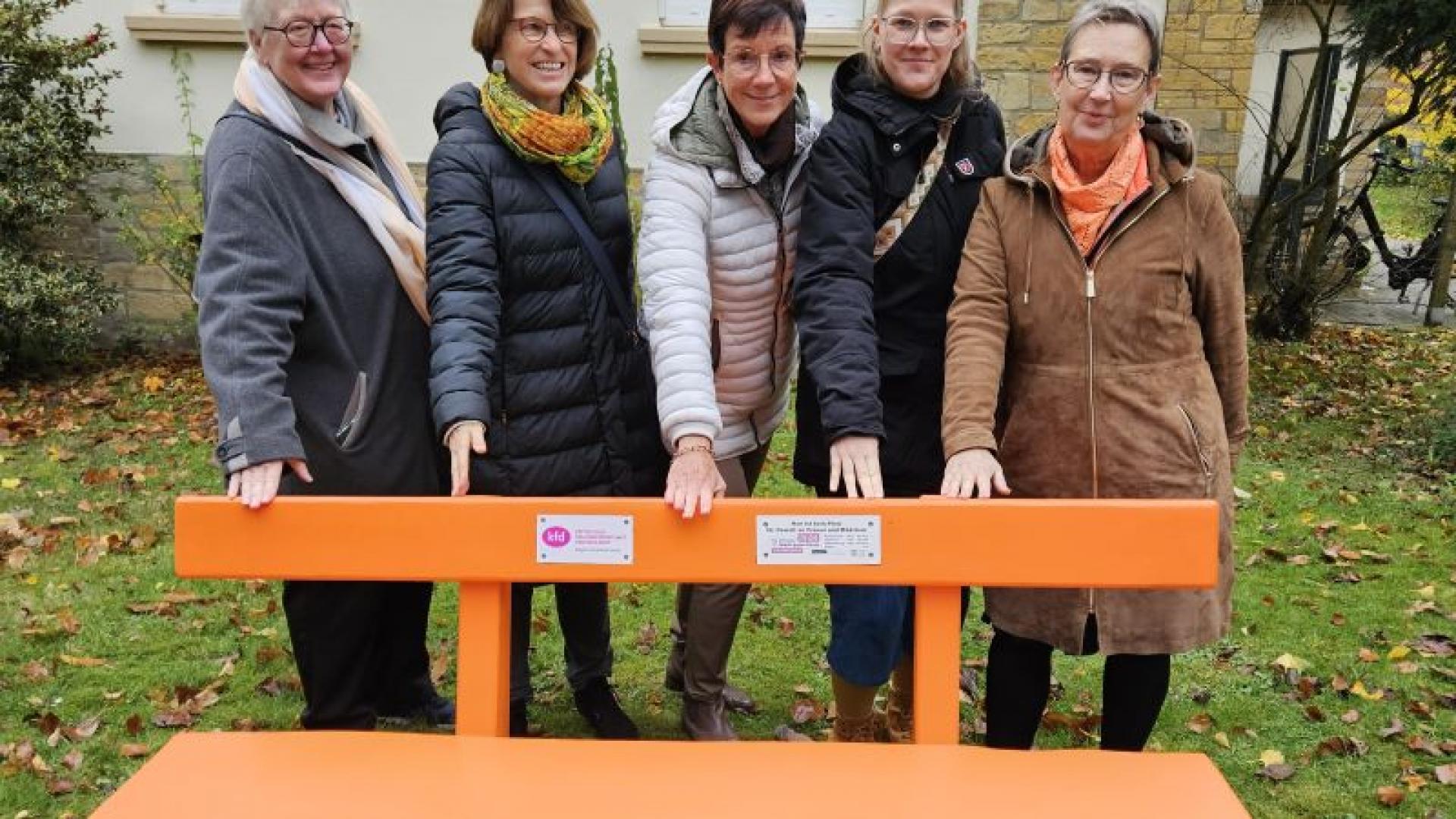 Fünf Frauen stehen hinter einer orangefarbenen Sitzbank