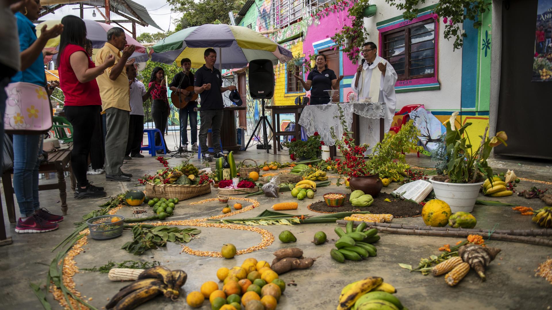 Menschen feiern draußen einen Gottesdienst, auf dem Boden liegen Früchte und andere Erntegaben 