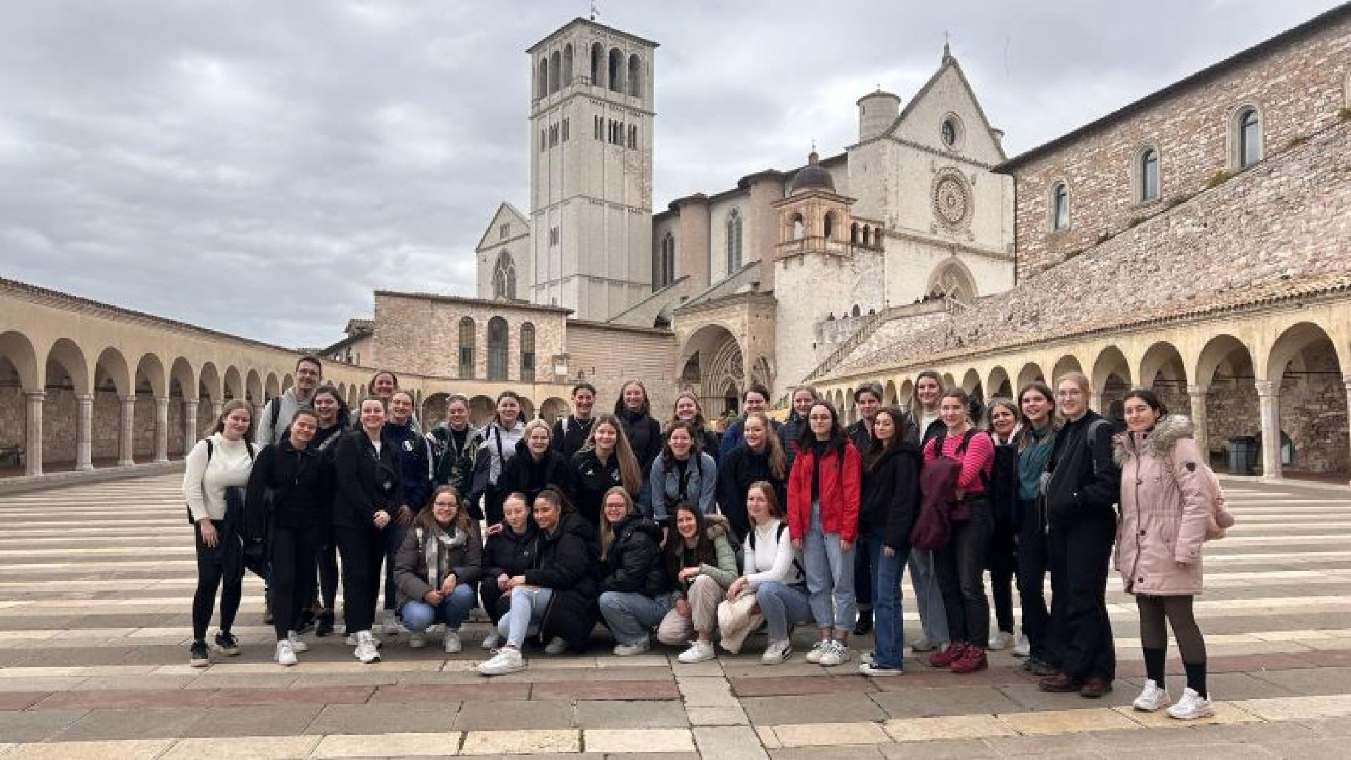 Junge Leute stehen auf einem Platz, im Hintergrund eine Kirche