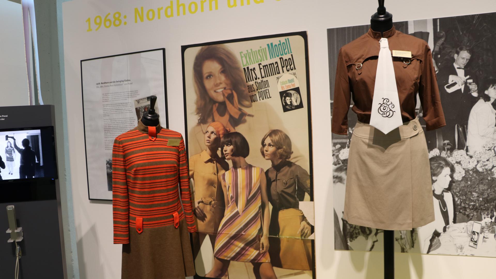 Ausstellungsnische mit Originalkleidern der Firma Povel aus der Emma-Peel-Kollektion, im Hintergrund hängt ein Foto der Schauspielerin Diana Rigg.