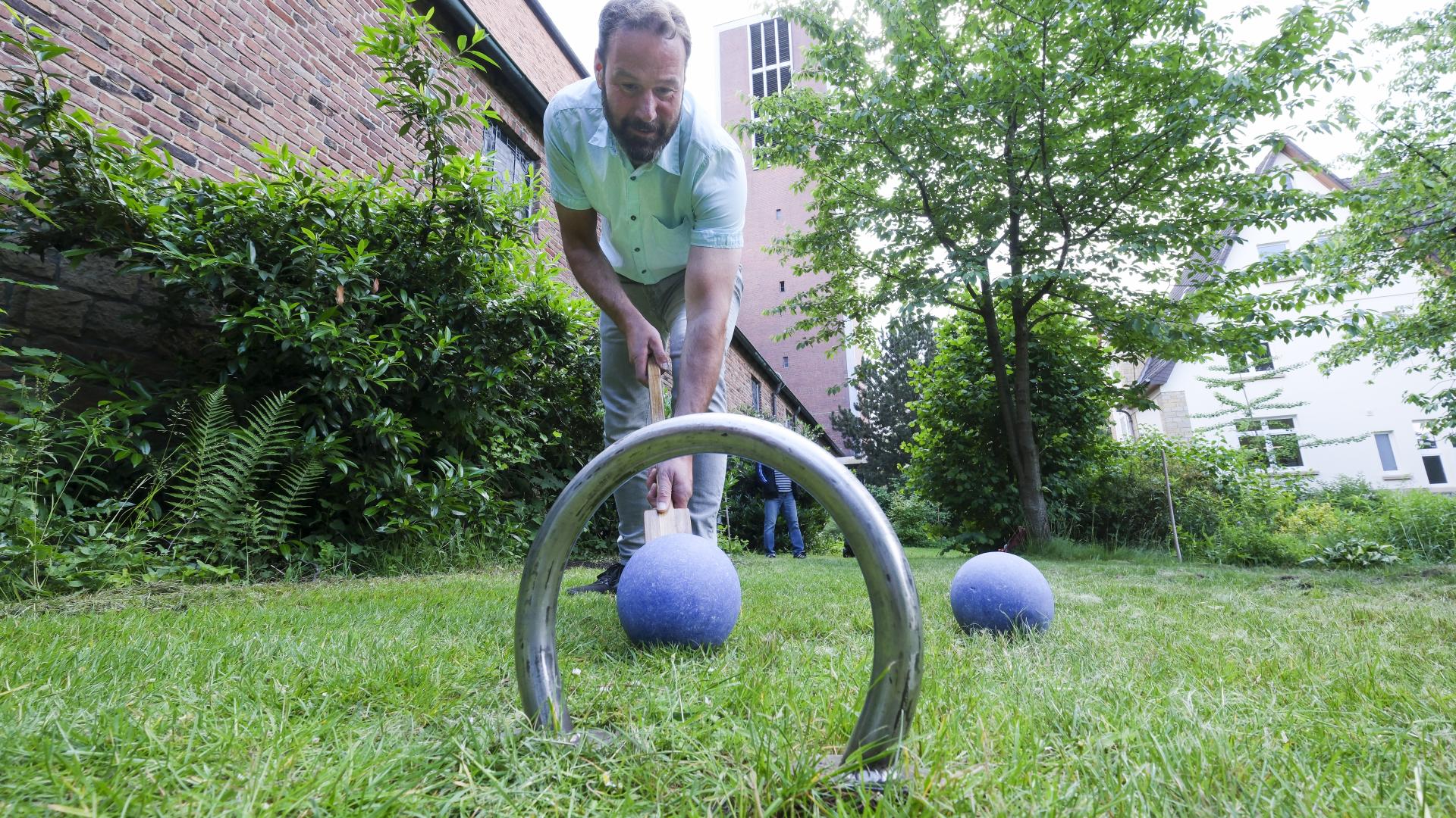 Ein Mann schiebt mithilfe eines Stocks eine blaue Kugel durch eine Rundung aus Metall