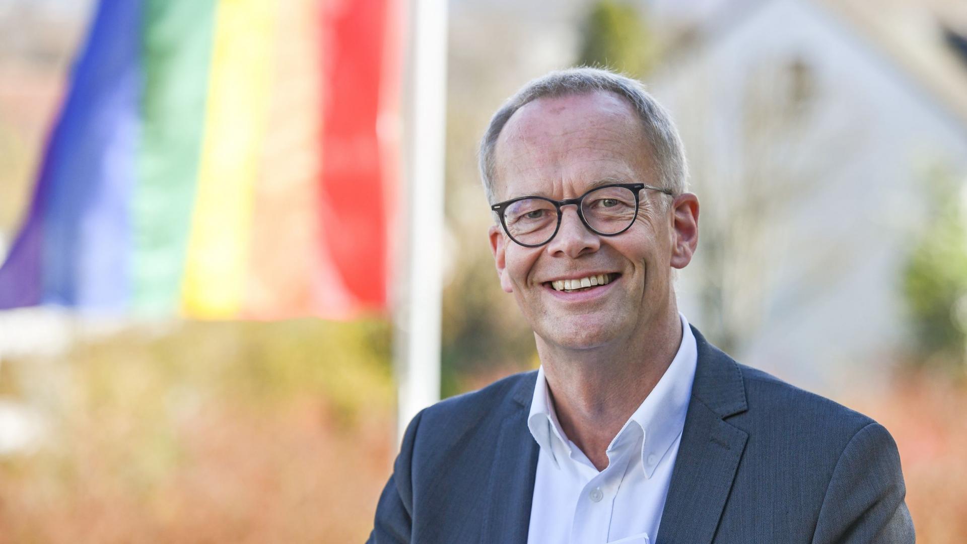 Burkhard Hose, im Hintergrund ist eine Regenbogenfahne