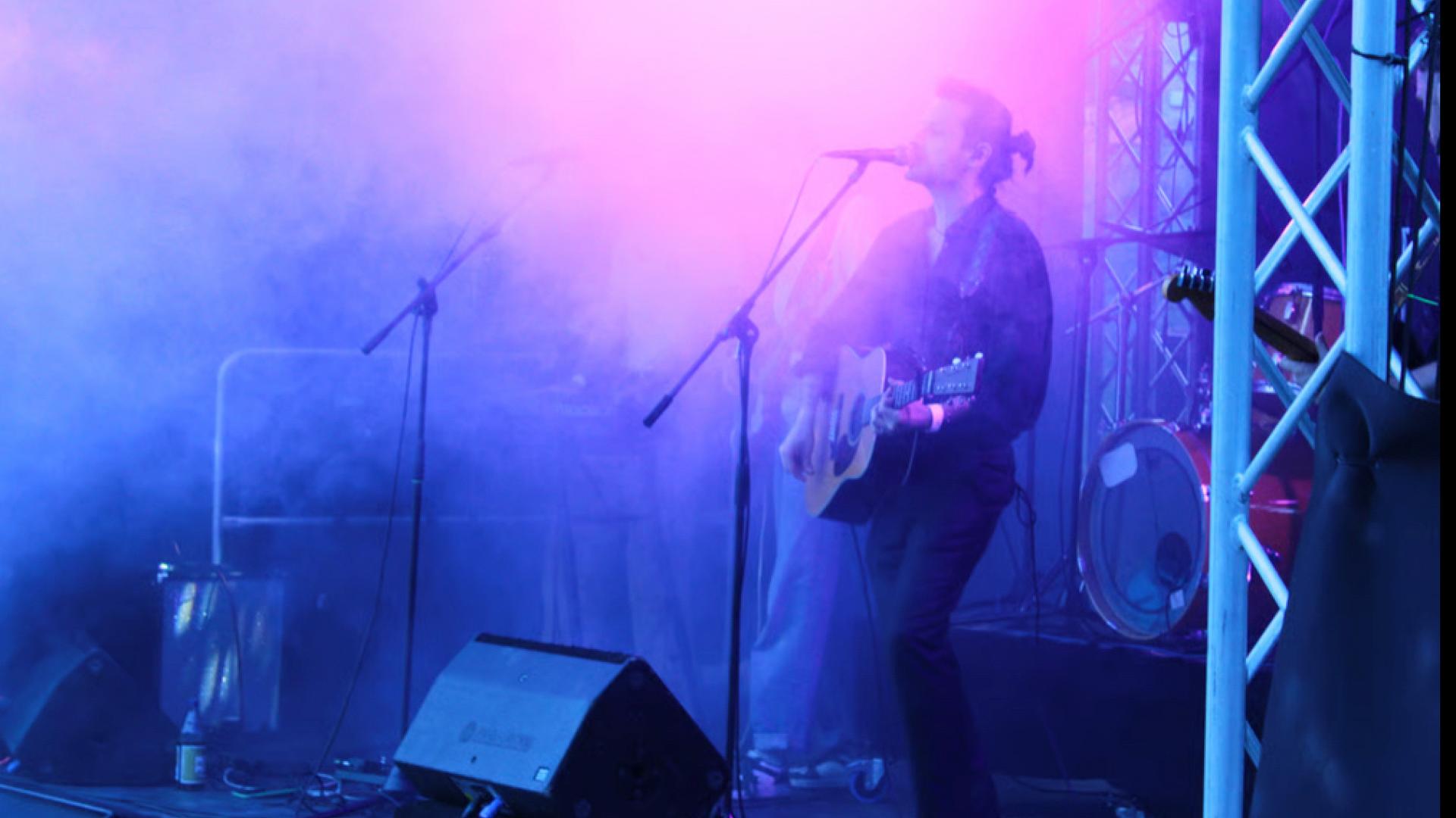 Sänger mit Gitarre auf vernebelter Bühne. 