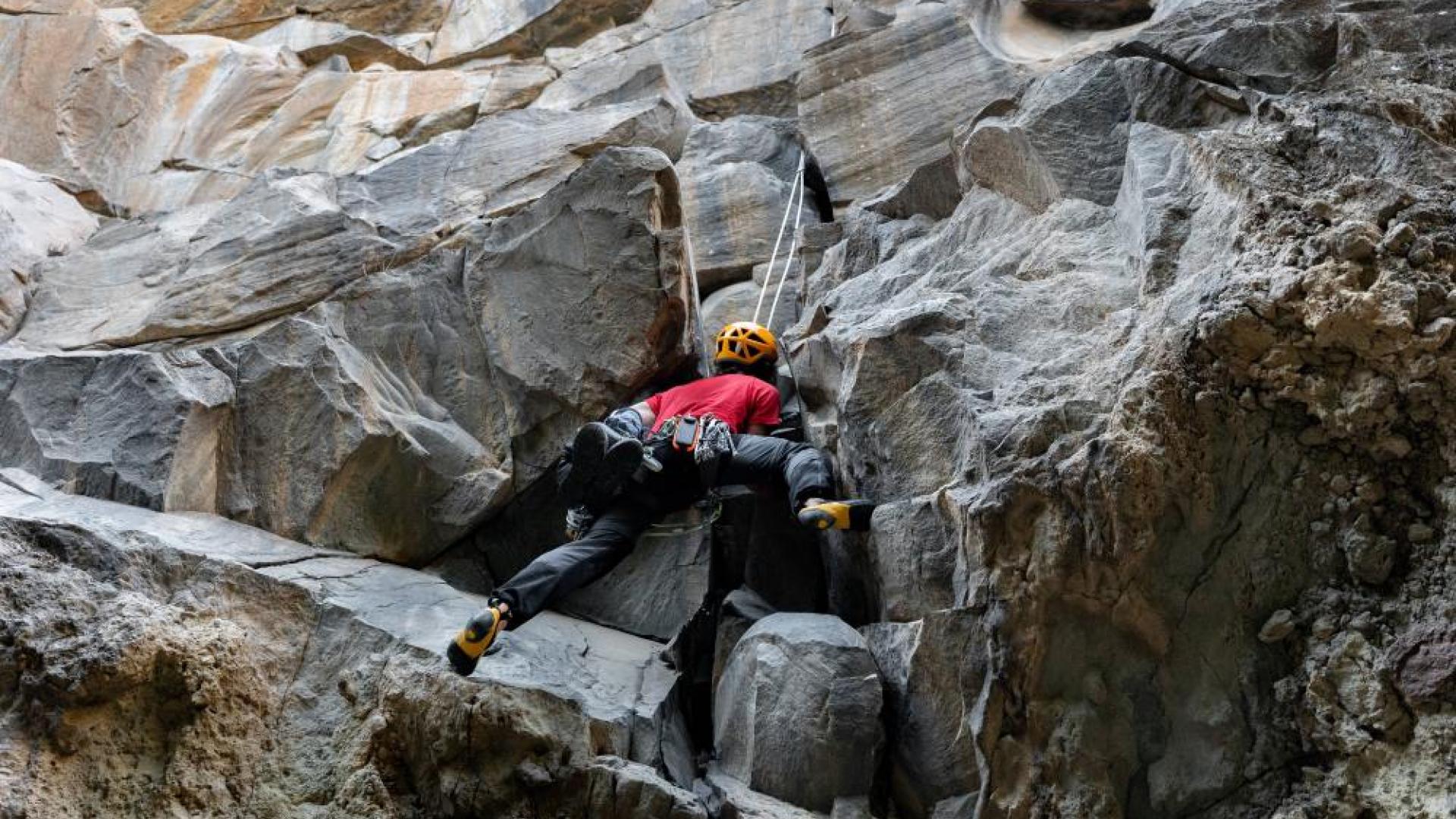 Ein Bergsteiger klettert mit einem Seil eine Felswand.