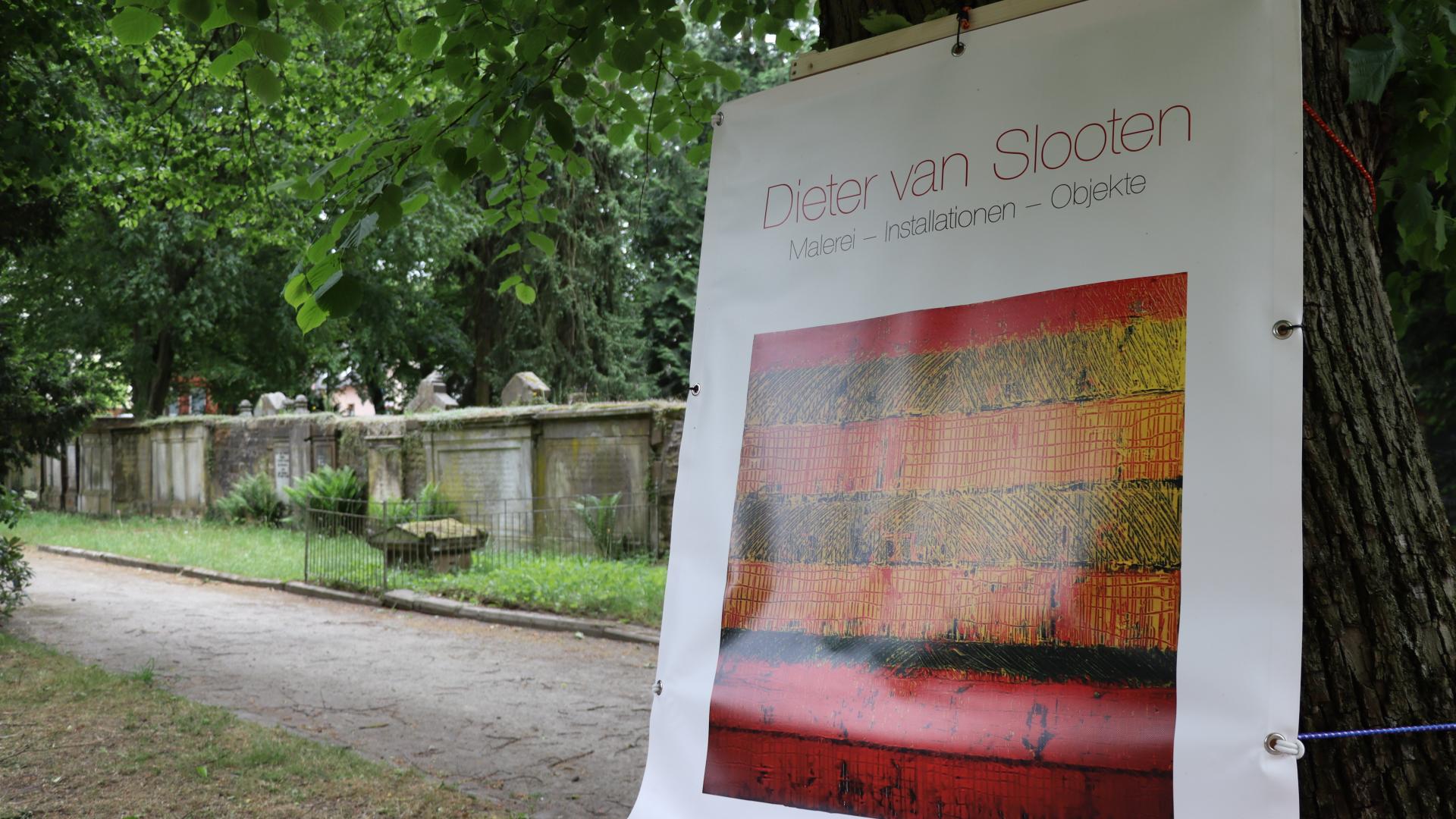 Eine Leinwand steht auf einer Staffelei auf einem Friedhof. Darauf ein Bild aus einer Kunstaustellung.