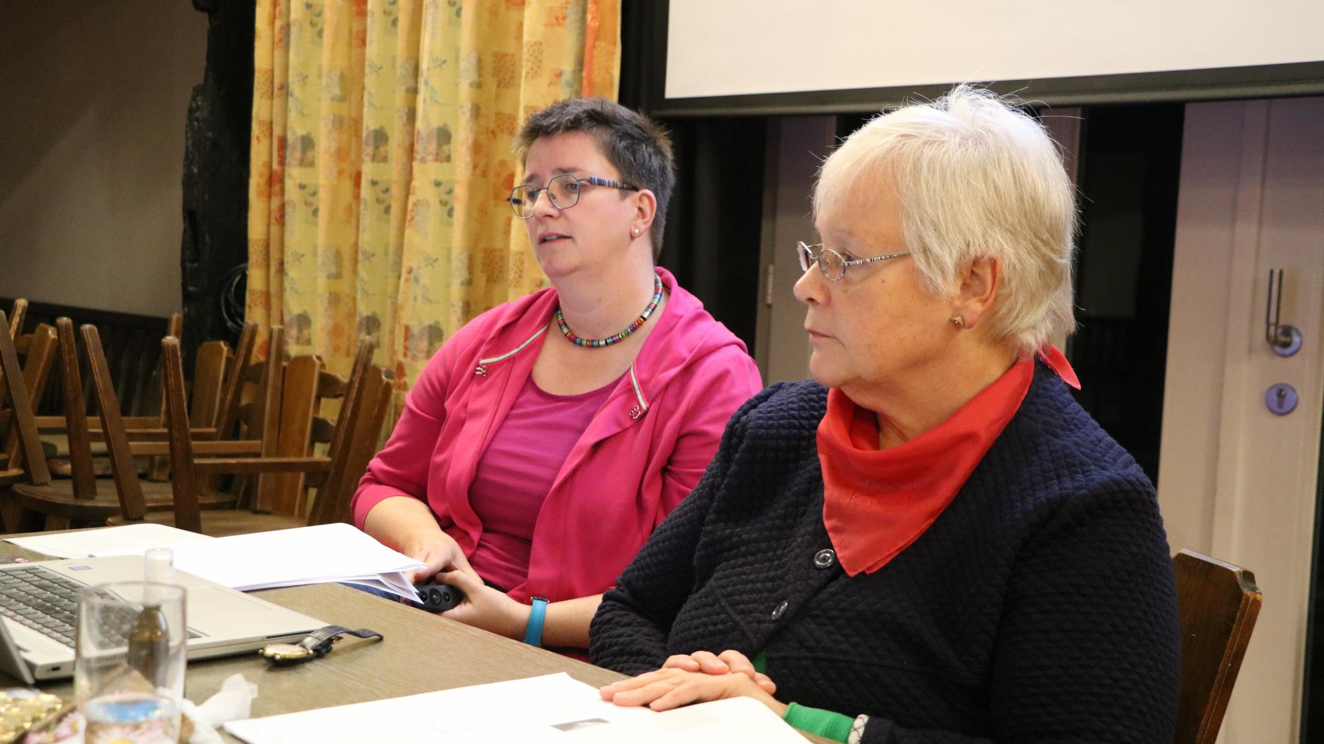 Zwei Frauen sitzen nebeneinander an einem Tisch. 