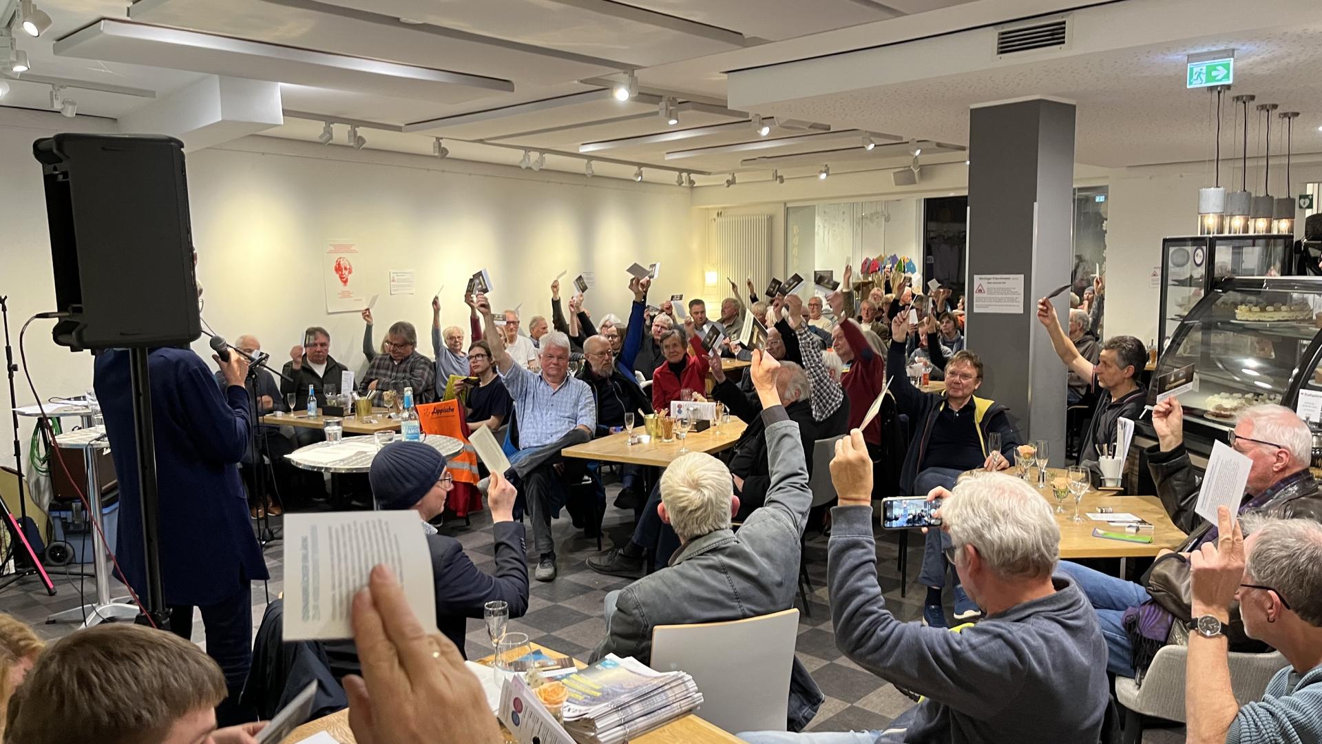 Eine große Menschengruppe sitzt an Tisch und viele halten eine Karte in die Höhe