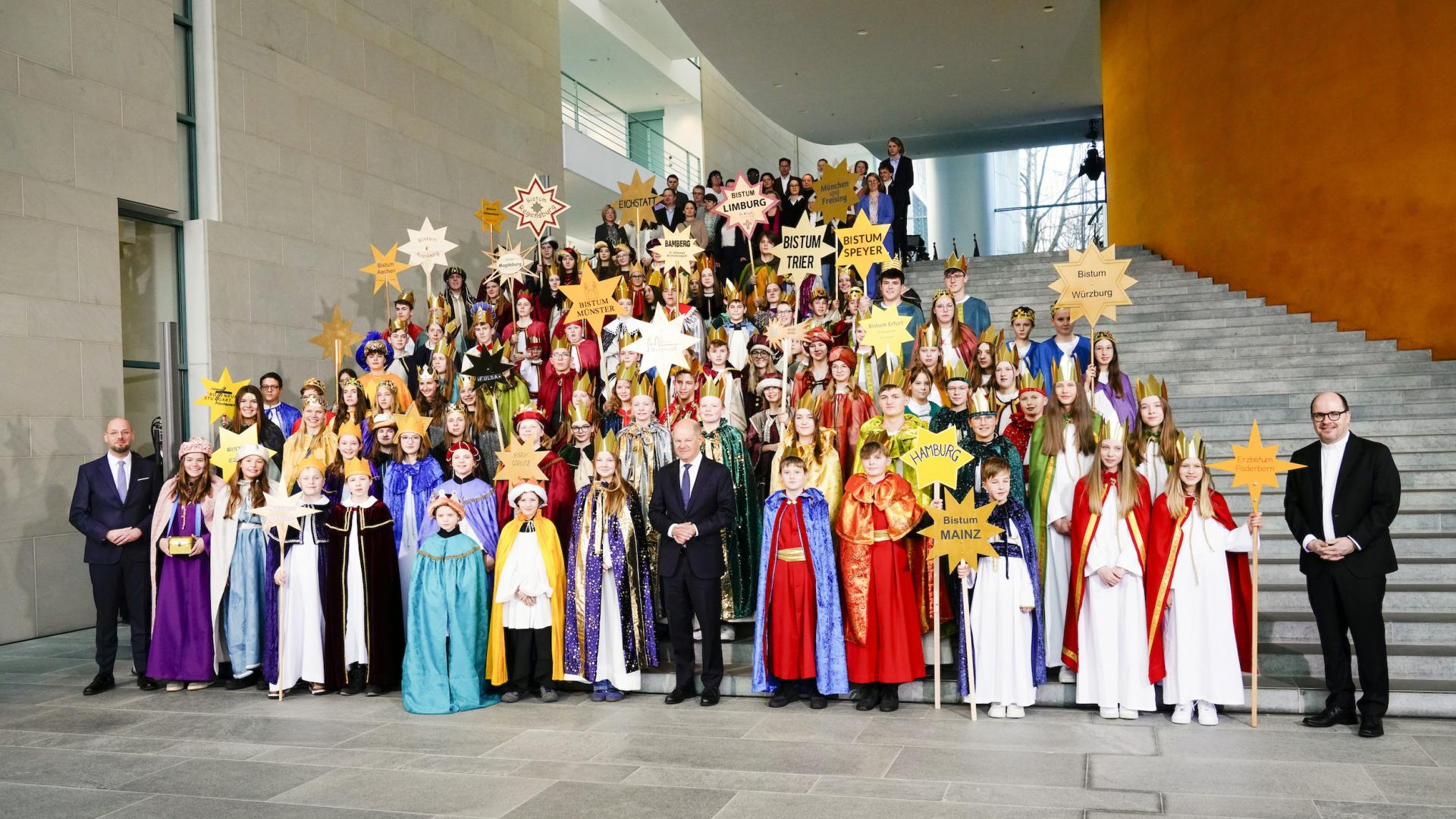 Eine große Kindergruppe als Sternsinger verkleidet. Mittendrin Bundeskanzler Scholz