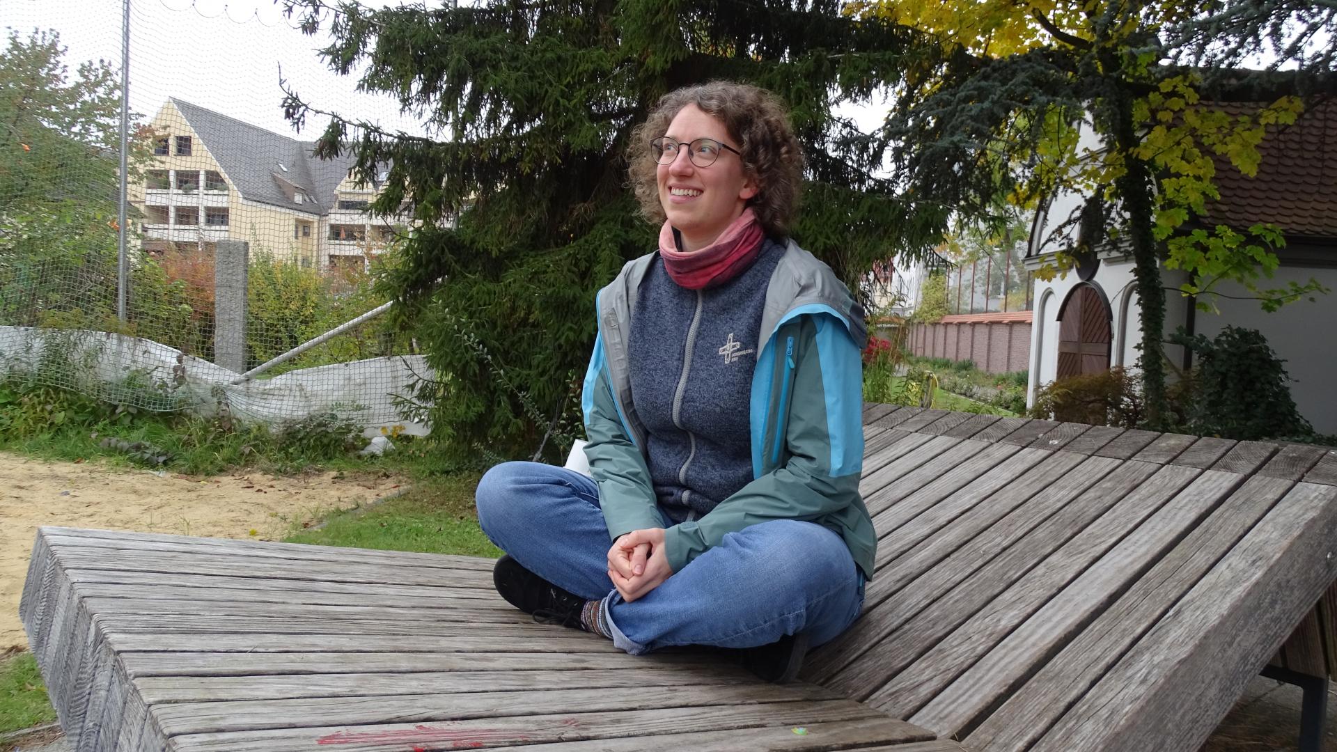 SChwester Salome sitzt auf einer Bank und lächelt in die Kamera, sie trägt Alltagskleidung.