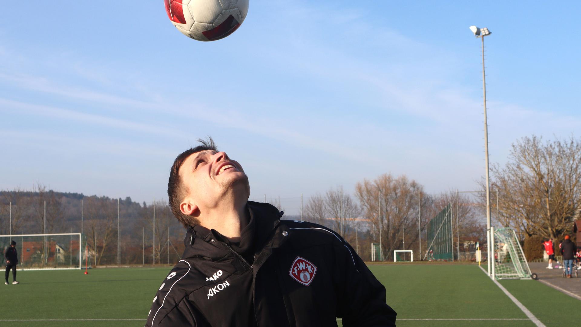 Jannik Feidel lässt einen Fußball auf seinem Kopf springen. Er steht in Fußballjacke auf einem Sportplatz.
