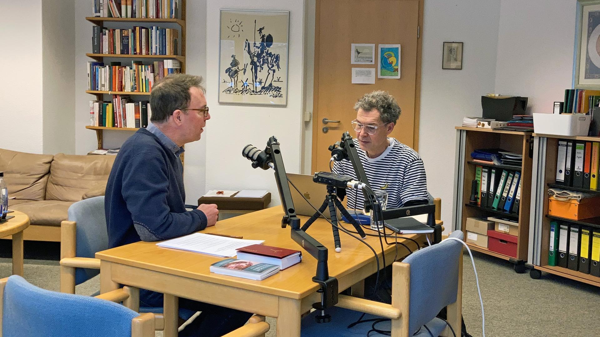  Zwei Männer sitzen an einem Tisch und sprechen in Mikrofone.