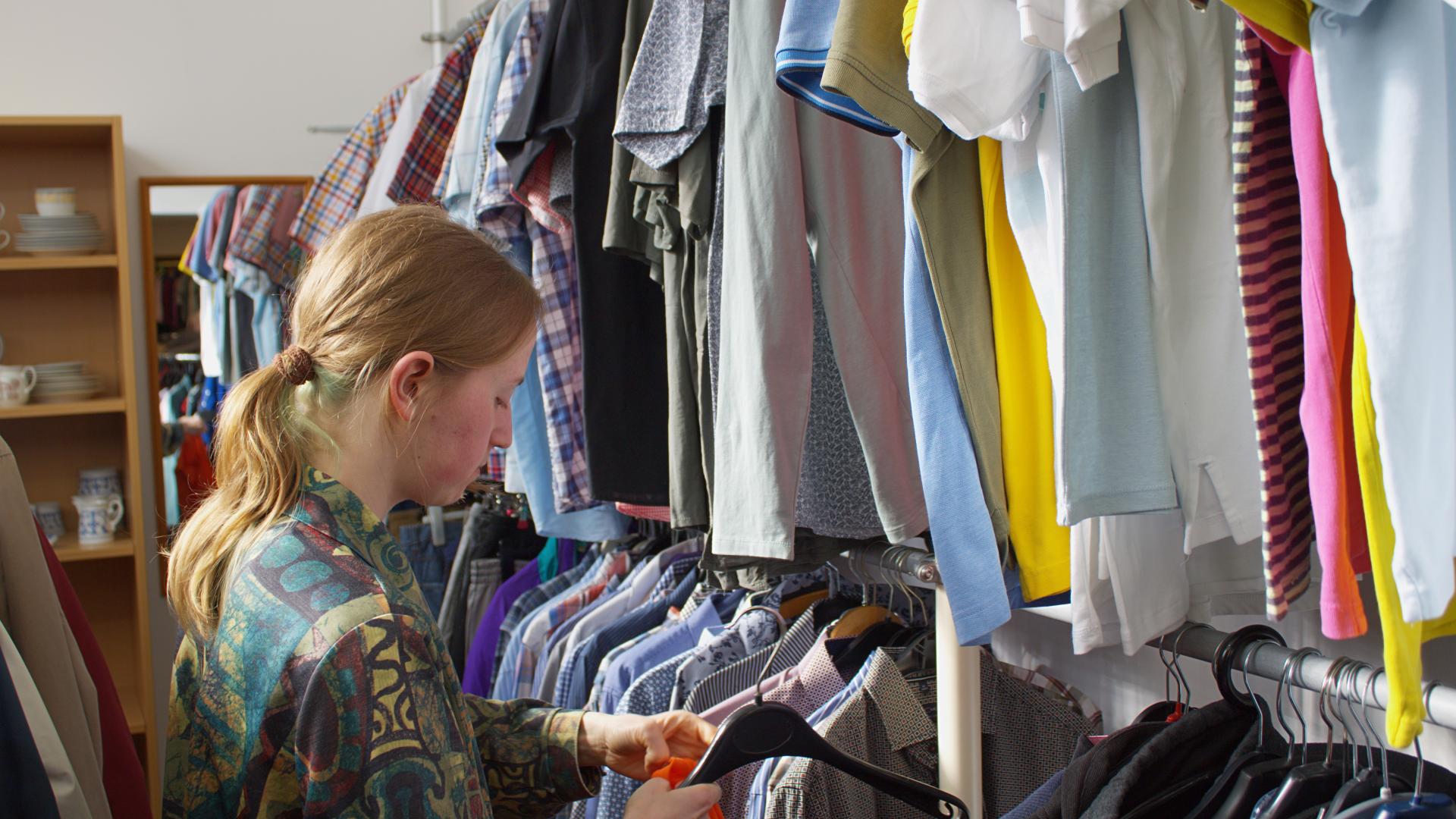 Ein junger Mann steht vor einem Kleiderregal