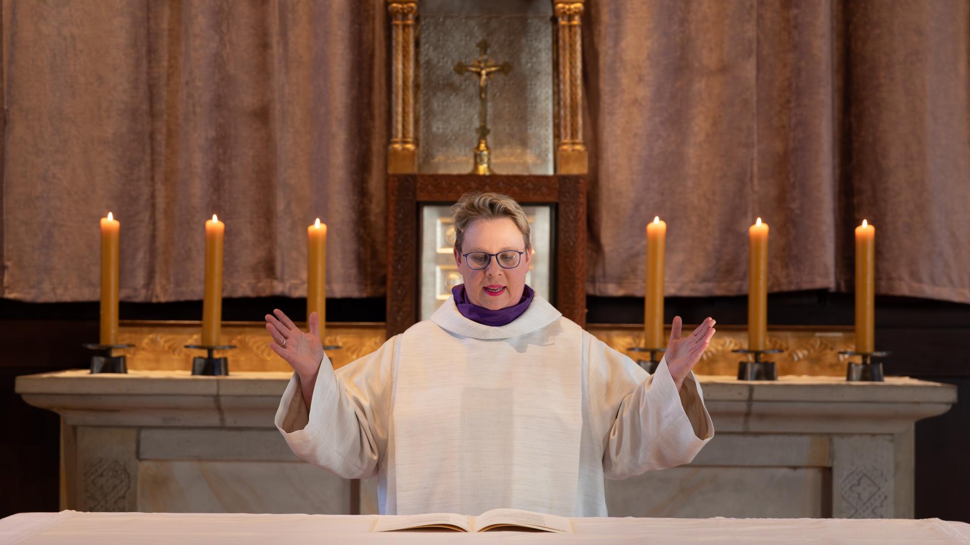 Eine Frau steht an einem Altar und breitet die Arme aus