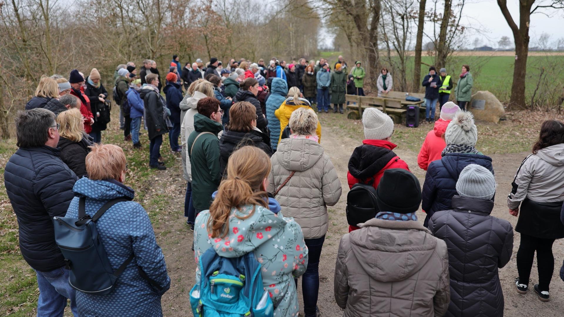 Eine größere Menschengruppe steht um ein Wegekreuz auf einem Feldweg