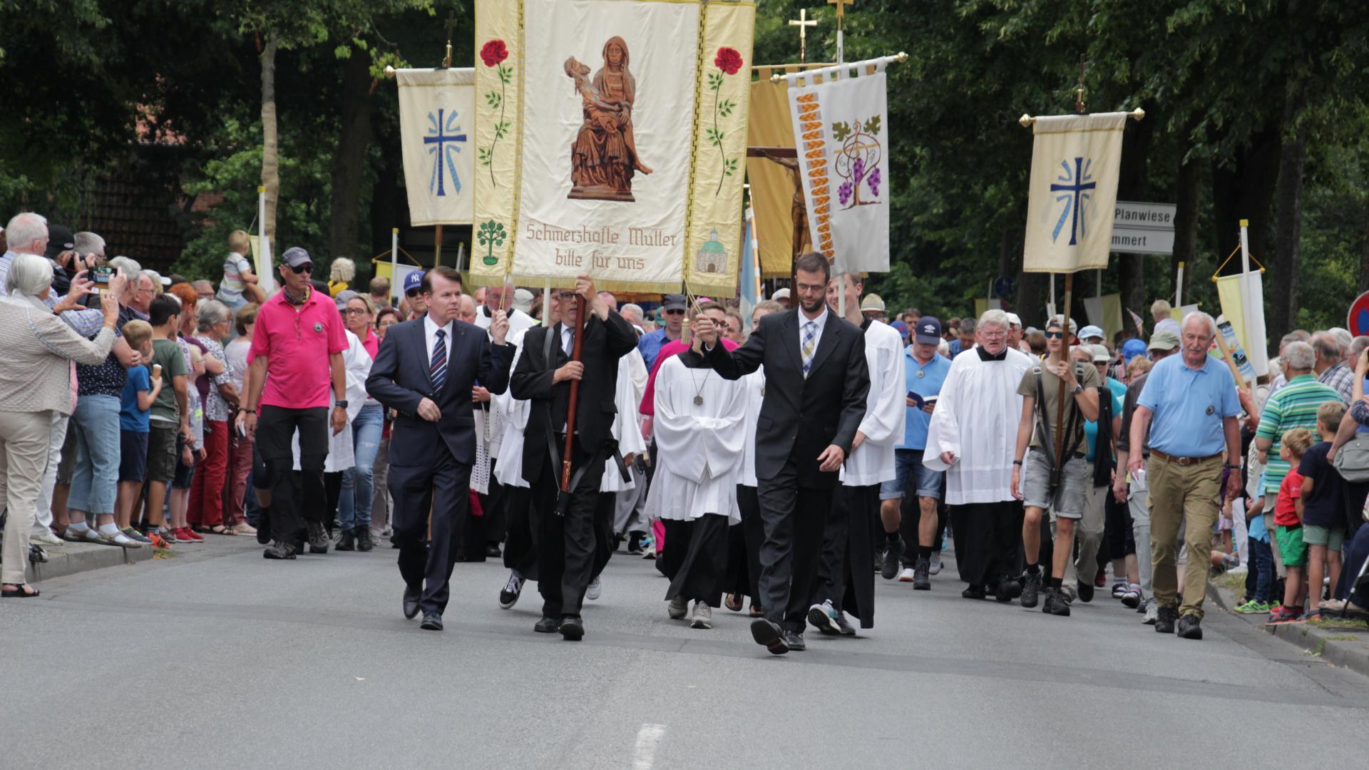 Eine große Menschenmenge geht zum Teil in liturgischer Kleidung auf einer Straße. Einige tragen Banner mit sich.
