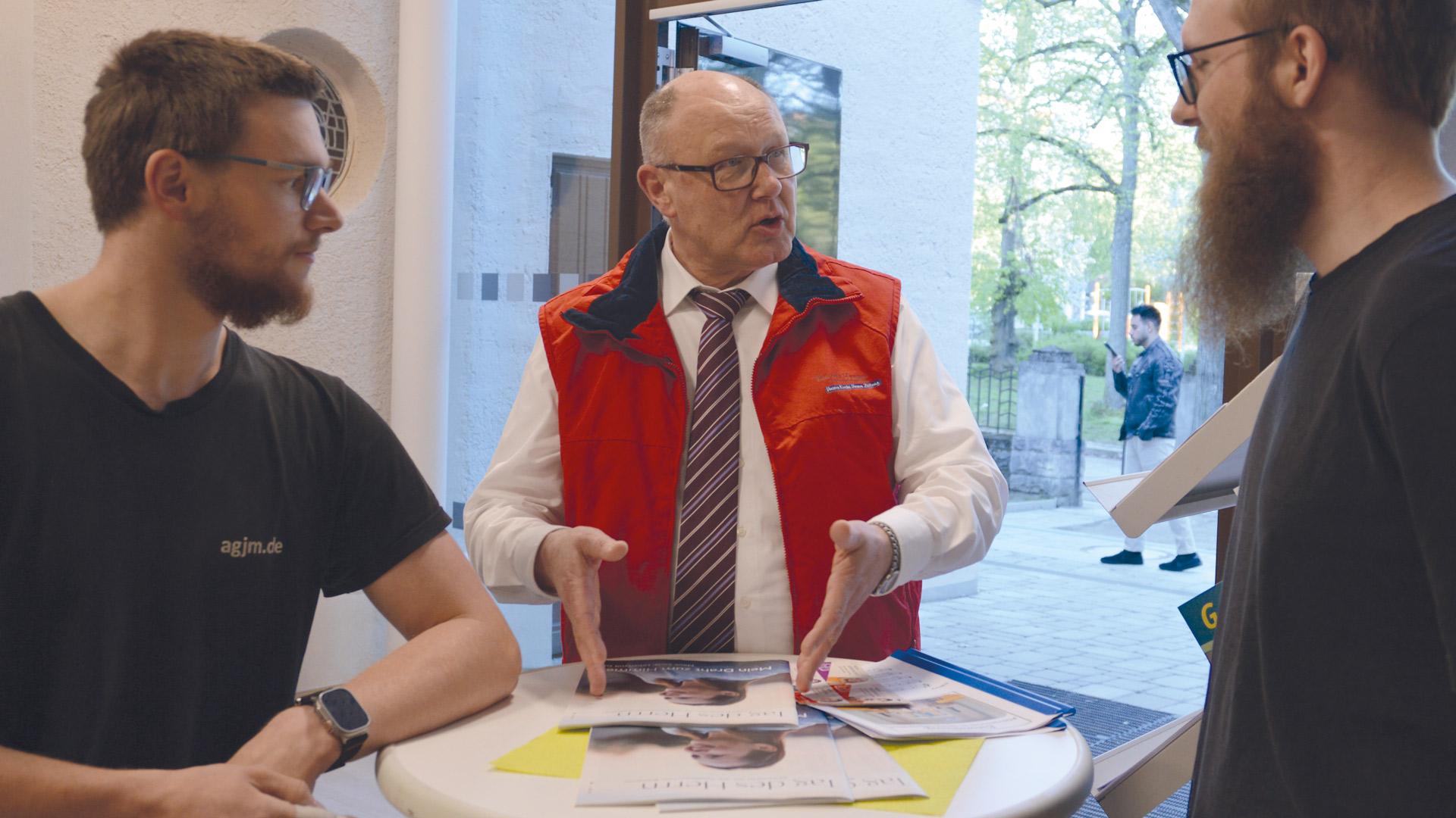 Willi Krug steht in der Mitte und spricht mit zwei Männern über den TAG DES HERRN