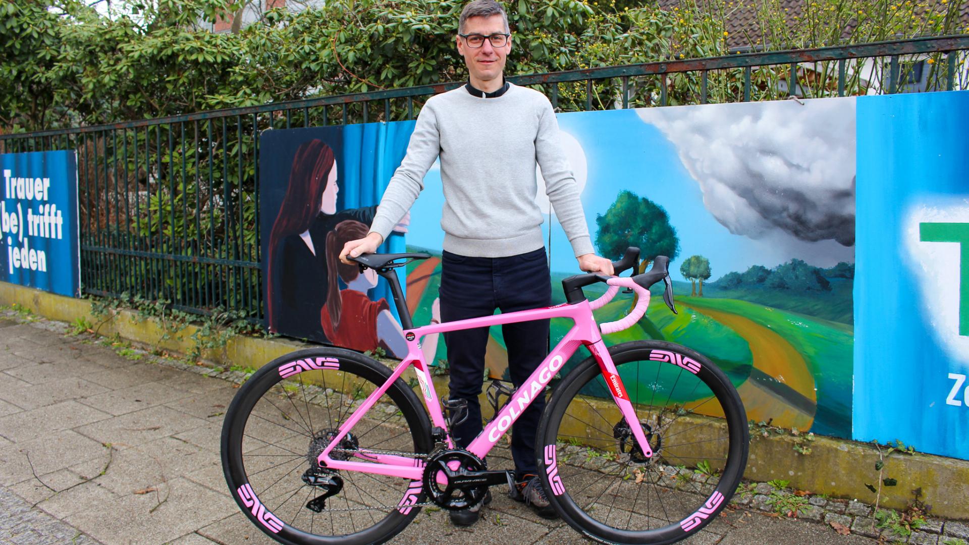 Ein Mann in Sportbekleidung steht hinter einem Rennrad