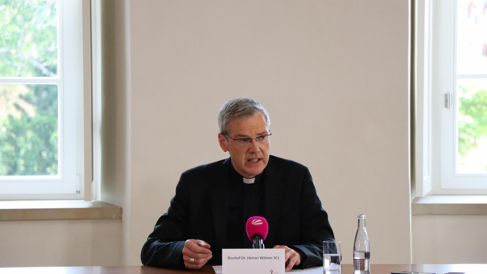Bischof Wilmer sitzt allein an einem Tisch, vor sich ein Mikrofon