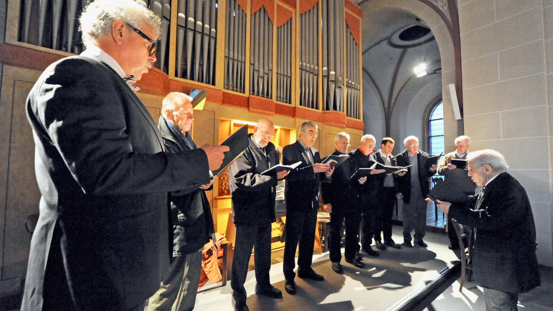 Männer singen im Chor vor einer Orgel.