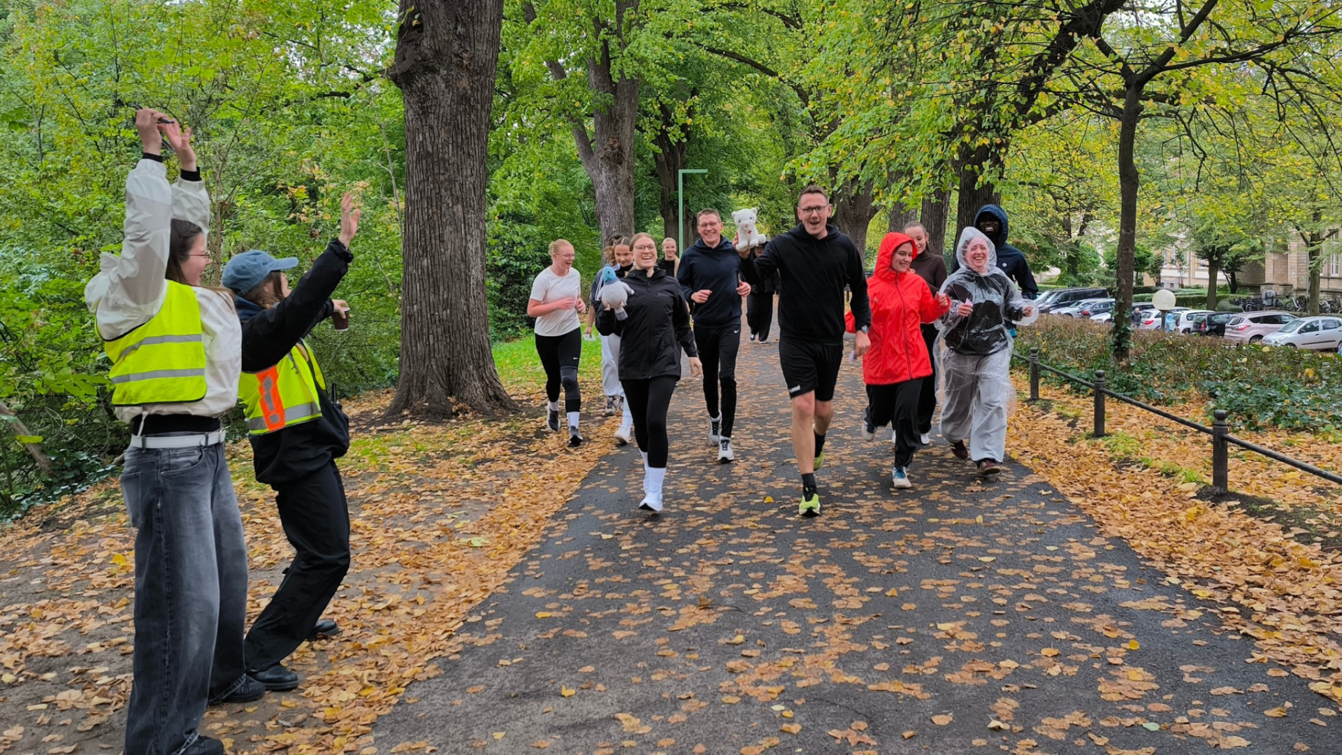 Eine Gruppe von Lehrern und Schülerinnen joggt auf einem Weg, daneben stehen zwei Schülerinne, die anfeuern