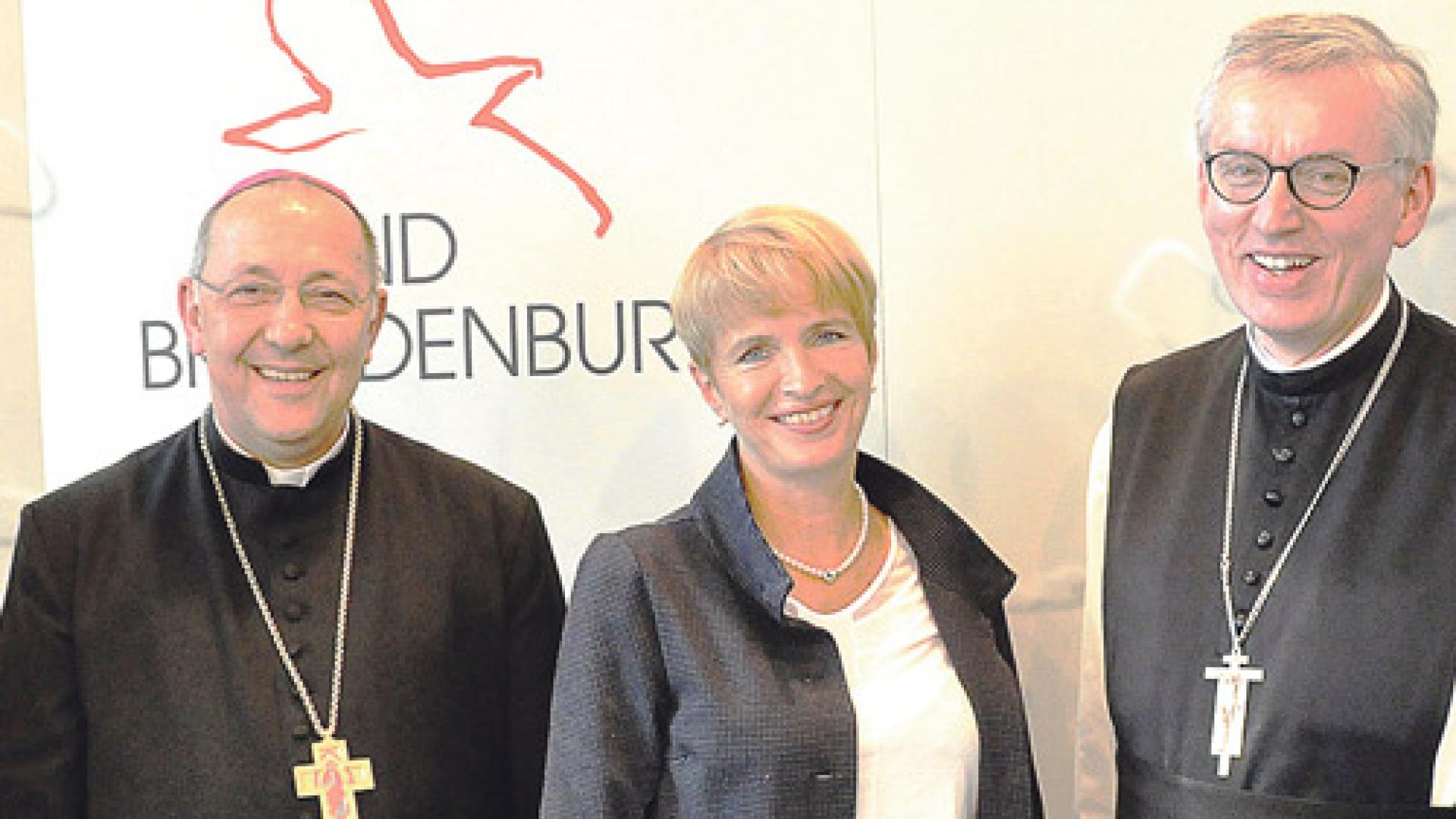 Drei Menschen stehen vor einer Wand. 